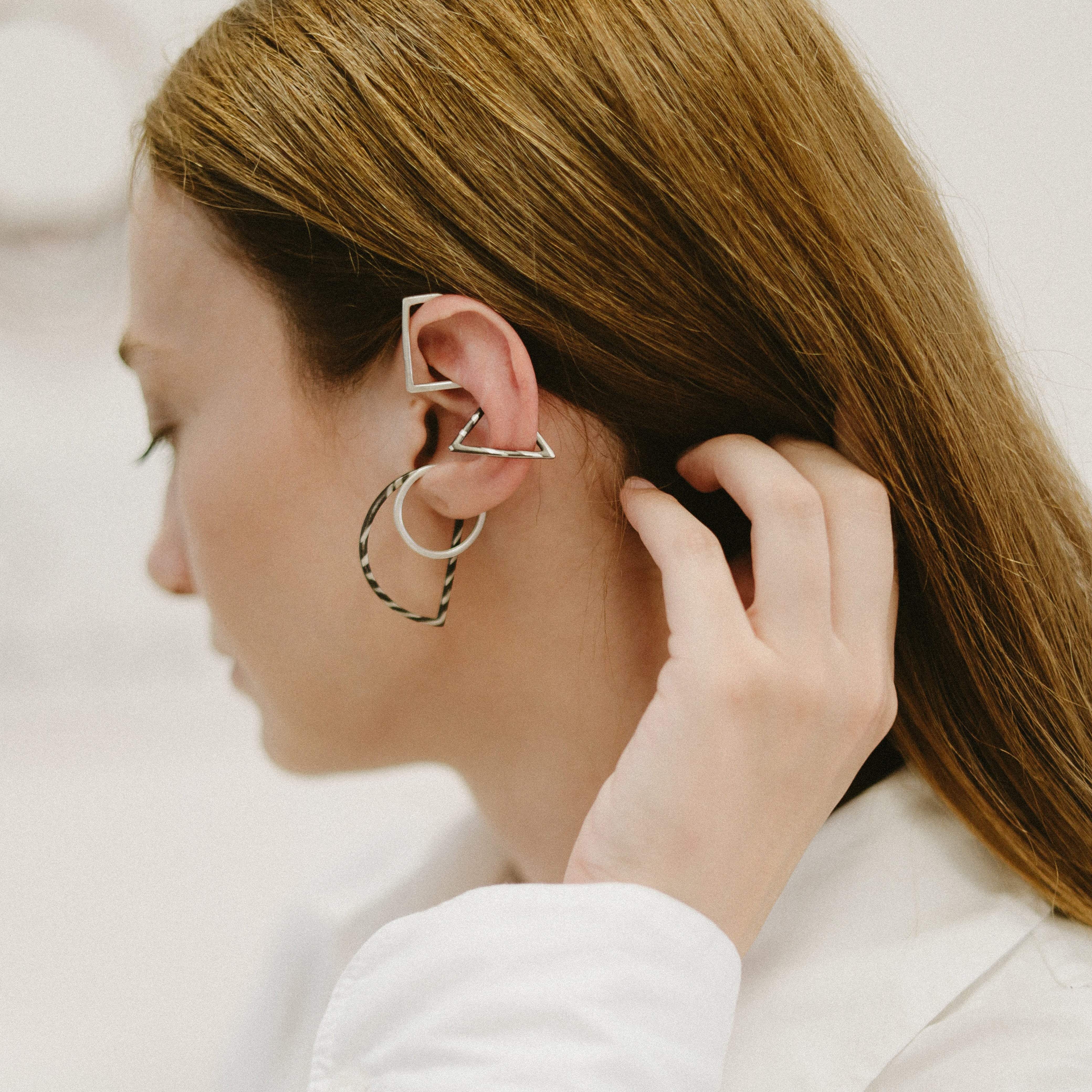 Person wearing multiple ear cuffs with a neutral background