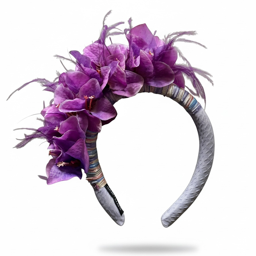 A decorative headband featuring a cluster of purple bougainvillea flowers and light gray feathers, wrapped with multicolored striped fabric and a textured gray band, shown on a white background.
