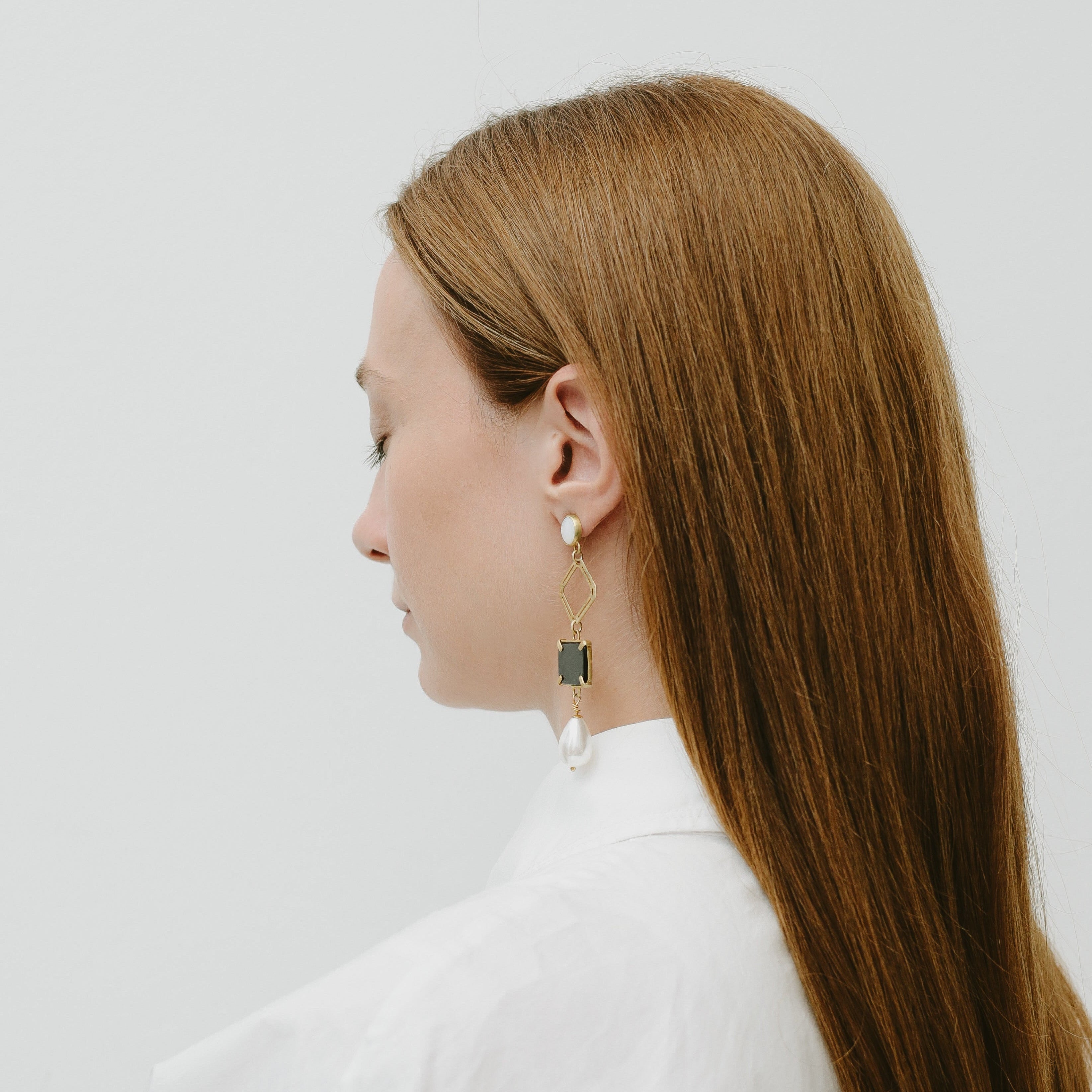Woman with long brown hair wearing earrings against a white background