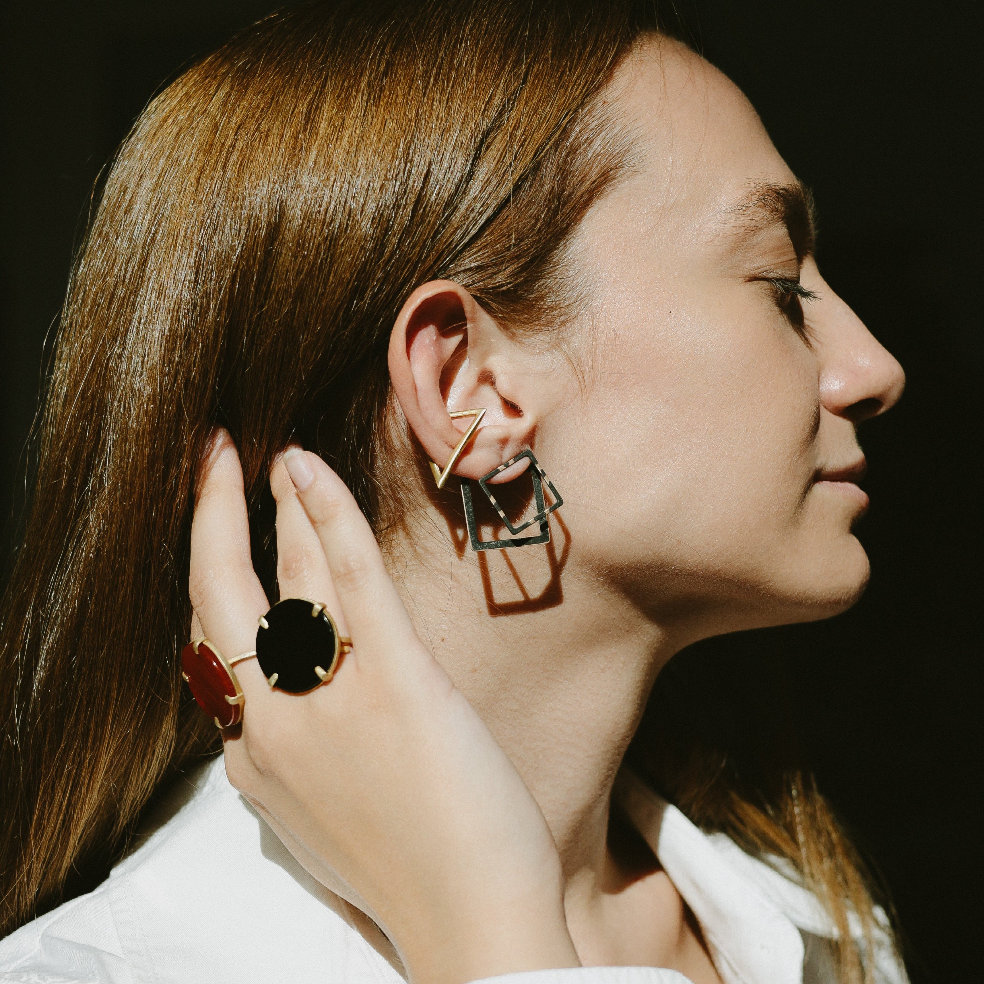 Woman wearing 2D earrings (aka ear-jackets) and ear cuffs with a dark background